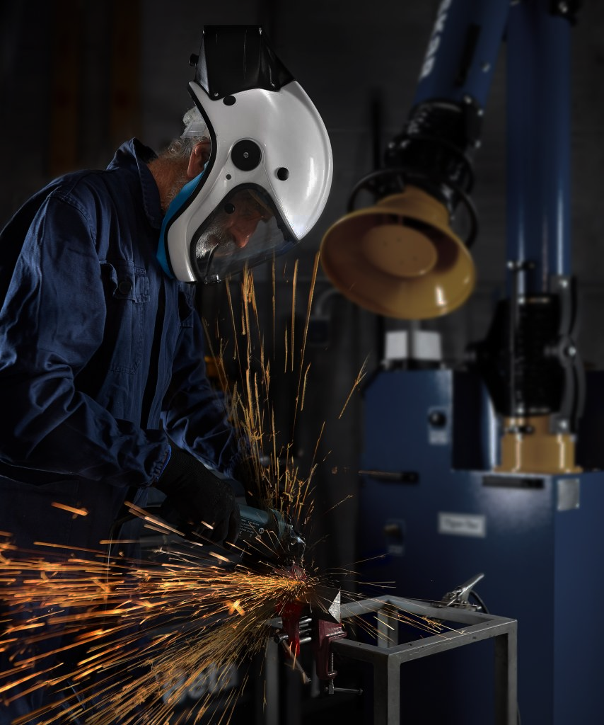 Un carpentiere metallico con tuta blu e casco bianco protettivo effettua una lavorazione metallica generando scintille