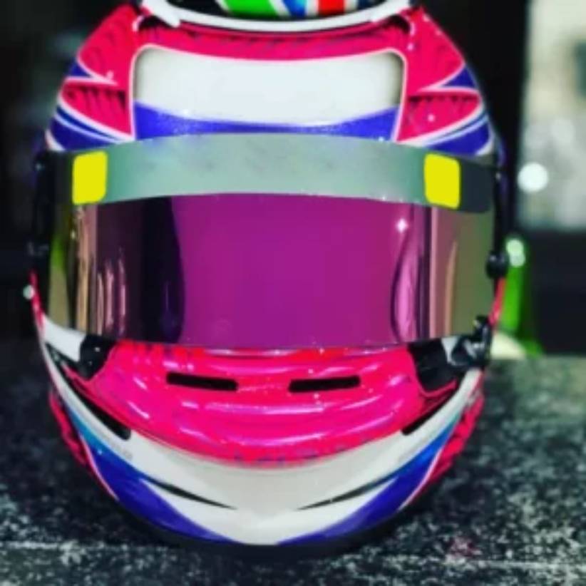 Foto frontale di un casco da kart viola, bianco e blu appoggiato su un ripiano in marmo scuro