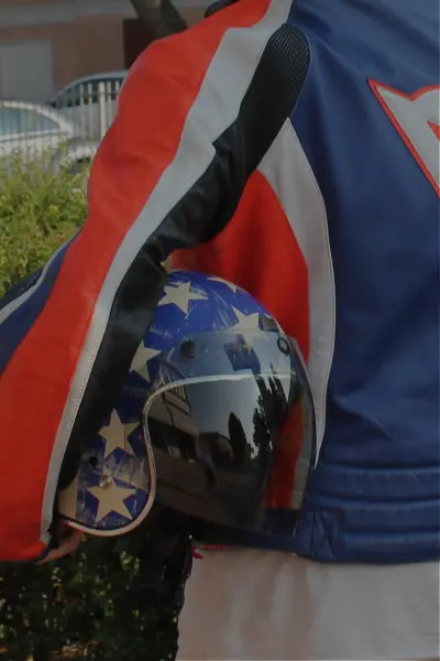 Vista da dietro di una persona che tiene tra le braccia un casco con la bandiera americana